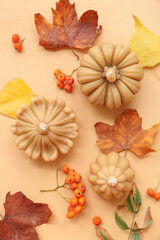 Beautiful composition with candles in shape of pumpkin and autumn leaves on beige background