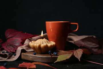 Beautiful autumn composition with burning candle in shape of pumpkin and cup of tea on black background