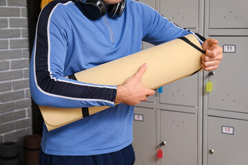 Sporty young man with fitness mat near locker in changing room, closeup