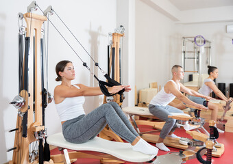 Willing young woman engaged in arm workout on cable type fitness equipment in exercise room