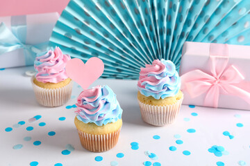 Delicious cupcakes with gift boxes and decorations on table against pink background. Gender reveal party concept