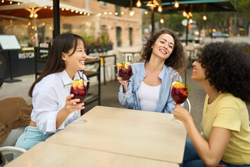 Three women are sitting at a table with drinks and smiling