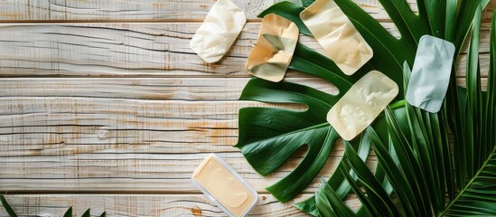 Flat lay on wooden surface featuring various under eye patch packages and a tropical leaf, with a blank area for text next to the products - a cosmetic item. Copy space image