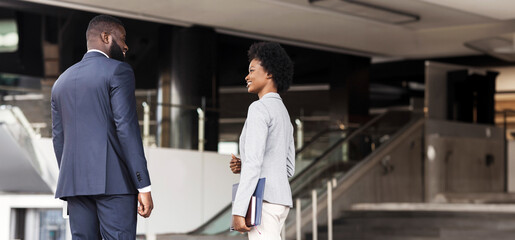 Attractive african american coworkers having pleasant chat while standing against office center, copy space