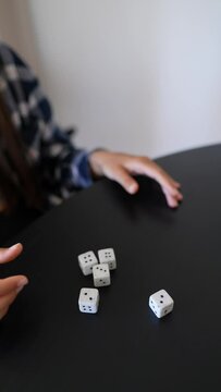 In the 4K footage, a woman is seen with a contemplative look as she rolls dice at a table
