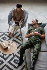 Vertical top view portrait of adult army veteran lying on couch in therapists office during...