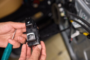A mechanics hands are seen repairing the cars interior door panel controller inside the vehicle
