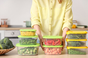 Woman holding plastic containers with vegetables for freezing in kitchen