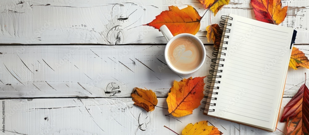 Poster autumn leaves and a coffee cup on a white grunge backdrop in a blank notebook with copy space image.