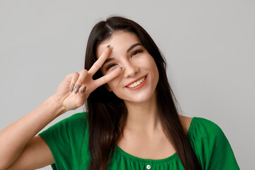 Young woman showing peace sign on light background, closeup