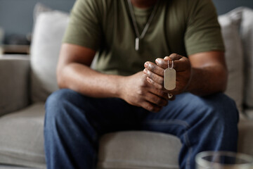 Closeup of African American man as army veteran holding dog tags necklace in hands during therapy session copy space
