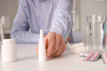 Ill businessman with nasal drops and pills on table in office, closeup