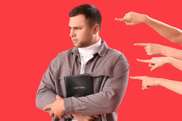 People pointing at young man with Holy Bible on red background. Accusation concept