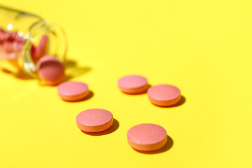 Overturned bottle with pills on yellow background, closeup