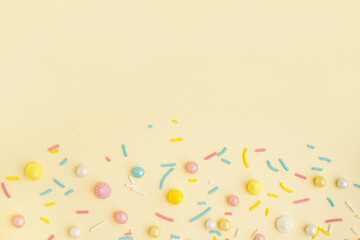 Sweet colorful sprinkles scattered on light yellow background