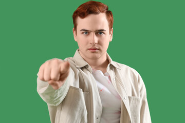 Young man pointing at viewer on green background, closeup. Accusation concept