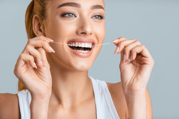 This image shows a woman flossing her teeth with a bright smile. Her bright white teeth and healthy smile are a great example of the importance of proper dental hygiene.