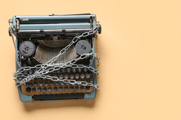 Vintage typewriter with chains on beige background. Printing ban concept