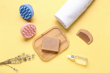 Hair scalp massagers with shampoo bar and cosmetic oil on yellow background