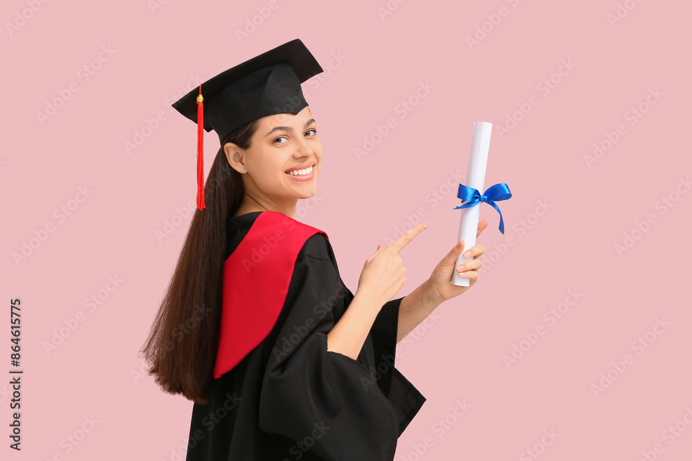 Wall mural Happy female graduate pointing at diploma on pink background