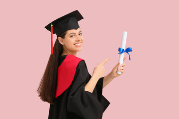 Happy female graduate pointing at diploma on pink background