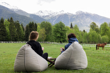 Two woman relax in a meadow overlooking the mountains in summer. High quality photo