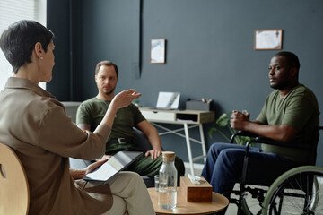 Over shoulder view of mature female therapist consulting two army veterans in therapy session dealing with PTSD and trauma copy space