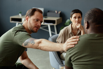 Portrait of army soldier comforting fellow veteran in group support therapy session with female therapist copy space
