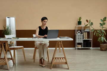Minimal wide angle portrait of successful mature woman using laptop at home office workplace in neutral colors copy space