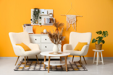 Stylish living room with white chest of drawers, pampas grass on coffee table, soft armchairs and pegboard