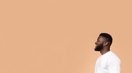 African American man smiling and looking off-camera, standing in front of a peach colored background. He is wearing a white t-shirt, panorama with copy space