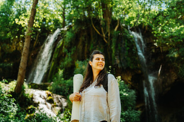 One young caucasian woman is taking a break from hiking near the river and waterfall in the forest	