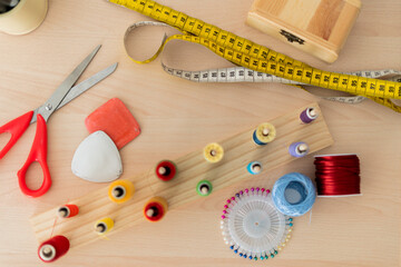 A variety of sewing tools and supplies neatly arranged on a wooden table, including scissors, measuring tape, thread spools, pins, and chalk for garment marking
