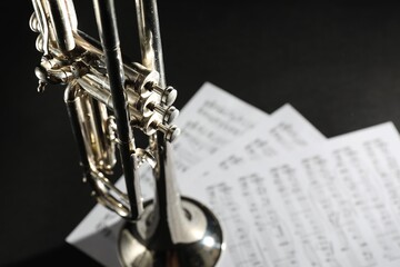 Closeup view of shiny trumpet and music sheets on dark background, space for text. Wind musical instrument © New Africa