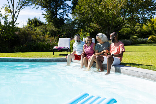 Group of senior friends sitting by pool, enjoying sunny day together