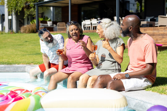 Diverse group of senior friends sitting by pool, enjoying drinks and laughing