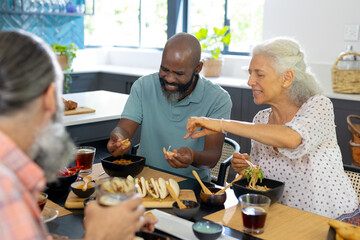 Eating together, diverse group of senior friends enjoying meal at home