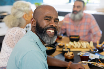 At home, Smiling man enjoying meal with senior friends at dining table, having fun