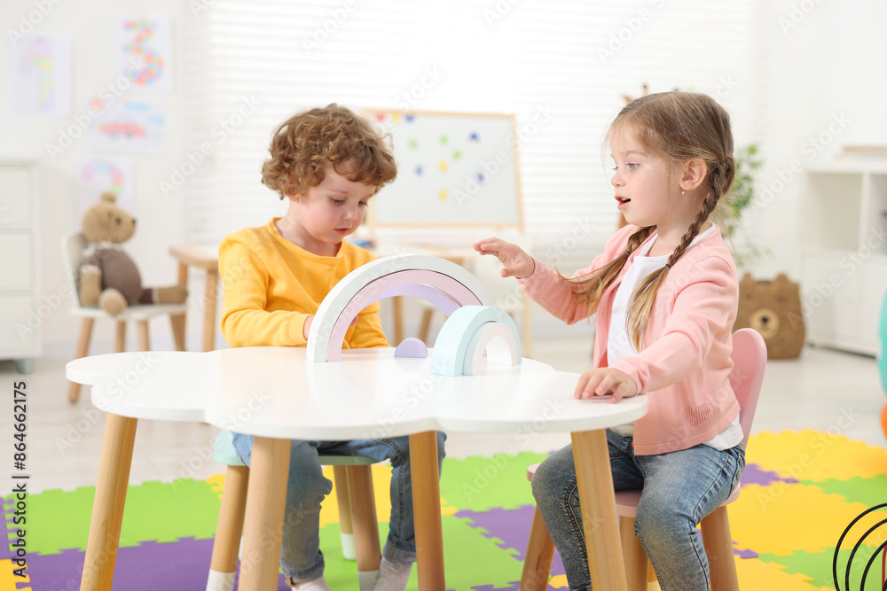 Wall mural Cute little children playing with colorful toy rainbow at white table in kindergarten