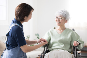 車椅子に乗るシニア女性と見つめ合う手を繋ぐ介護士の様子　訪問看護や通所介護(デイサービス)介護の求人や転職、のイメージに