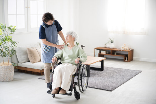 A caregiver pushing a wheelchair at home and a senior woman looking at each other Full body image for home nursing and day care (day service) care jobs and career change.Copy space on the right - Powered by Adobe