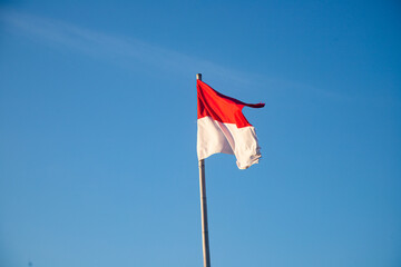 The red and white Indonesian flag flies at the end of a bamboo pole against a bright blue sky. Indonesian Independence day.