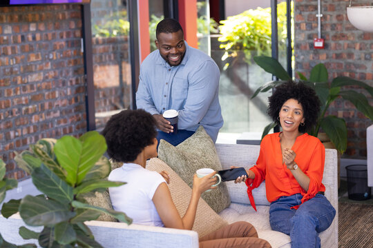 Diverse group of business colleagues discussing work, holding coffee cups in office