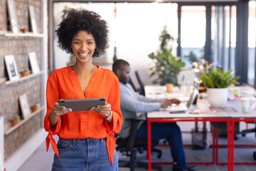 Holding tablet, female business professional smiling in modern office setting