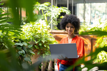 Holding laptop, African American businesswoman working in lush green office setting