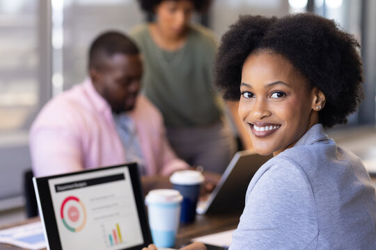 Smiling businesswoman with laptop showing financial charts in casual office meeting