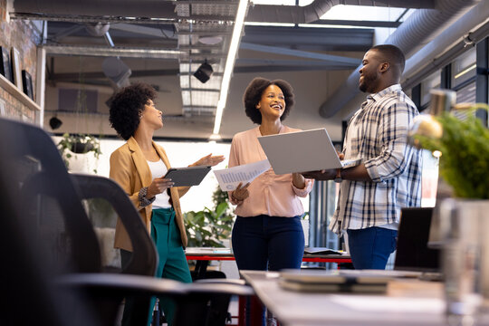 Business team discussing project, holding laptops and documents in modern office