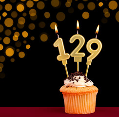 Birthday candle with cupcake - Number 129 on black background with out of focus lights