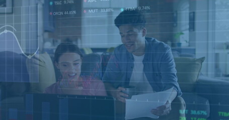 Image of multiple graphs and trading board over diverse couple checking expenses on laptop