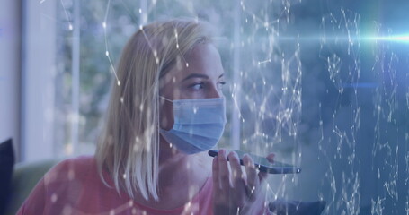 Image of moving shapes over caucasian woman with face mask using smartphone